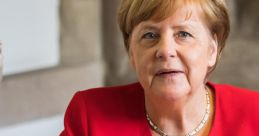 Angela Merkel in a red blazer, writing in a book during a formal event, showcasing her leadership and poise.