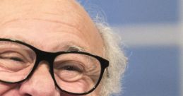 Danny DeVito smiling warmly, wearing glasses, showcasing his charming personality during a light-hearted interview.