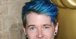 DanTDM smiles at an event, showcasing his signature blue hair and stylish attire, highlighting his vlogger persona.