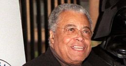 James Earl Jones smiling at an event, with a Darth Vader figure in the background, showcasing a legendary voice.