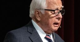 David McCullough speaking at an event, holding a book, showcasing his contribution to historical literature.