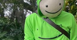 Dream wearing a signature green hoodie with a smiley face, standing among lush greenery, showcasing his iconic style.