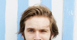 Felix "Pewdiepie" Kjellberg winks playfully, wearing a dark jacket against a blue and white striped background.