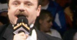 Howard Finkel, legendary wrestling announcer, speaking into a microphone with a crowd in the background during a match.