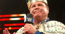 Jerry "The King" Lawler, wearing a crown and royal cape, gestures while speaking on stage at a wrestling event.