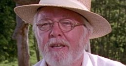 John Hammond, the visionary founder of Jurassic Park, in a straw hat and white shirt, surrounded by lush greenery.