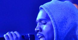 Kanye West performing passionately in a blue-lit setting, wearing a hoodie and holding a microphone.