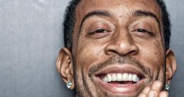 Ludacris smiles widely, hands clasped together, showcasing his signature style and charisma as a leading rapper.