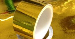 Glossy gold tape rolls on a shiny gold surface, perfect for crafts and decorating. Ideal for adding a touch of elegance.