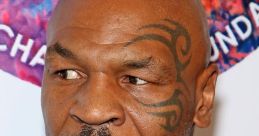 Mike Tyson with intense expression, showcasing his facial tattoo, dressed in a light blue suit at a public event.