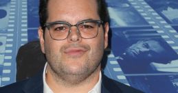 Josh Gad at an event, known for voicing Olaf in Frozen, wearing a blue suit and glasses with a confident expression.