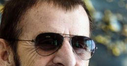 Ringo Starr smiles while wearing sunglasses and a denim jacket, showcasing his signature style and iconic persona.