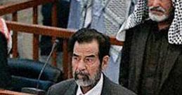 Saddam Hussein stands in court holding a book, surrounded by men in traditional attire, capturing a significant historical moment.