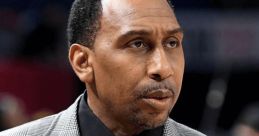 Stephen A. Smith in a stylish plaid suit, engaged in intense sports commentary at a basketball event.