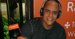 Waldemaro Martinez, radio host, gives a thumbs up while wearing headphones in a vibrant studio setting.