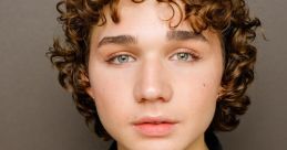 Portrait of young male with curly hair and green eyes, wearing a black jacket and green shirt, showcasing youthful charm.