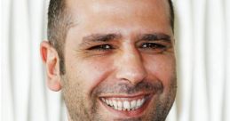 Checco Zalone smiling in a black jacket against a textured white background, showcasing his charismatic personality.