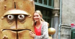 Woman poses with Bernd das Brot statue, a beloved character known for its humorous and moody personality, in a city setting.