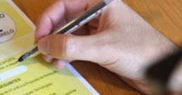 Hand holding a pen writing on a yellow exam sheet with guidelines, highlighting details for the "prova" process.