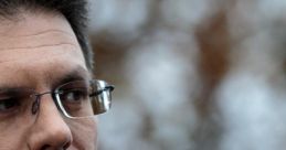 Steve Baker in a formal suit, thoughtfully gazing with an intense expression, set against a blurred natural background.