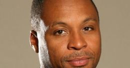 Professional headshot of Gus Johnson, showcasing his polished look with a black suit and purple tie against a neutral background.