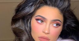 Kylie Jenner flaunts glamorous makeup and wavy hair, wearing a cozy pink robe in a chic, indoor setting.