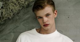 Young model wearing a stylish white oversized t-shirt with colorful graphic design against a textured wall backdrop.