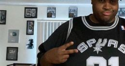 Man in a black Spurs jersey poses with peace sign, showcasing sports fandom in a cozy indoor setting.