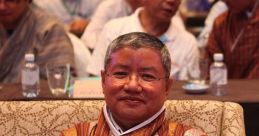 Kelzang Dorji seated at a conference, wearing traditional Bhutanese attire, engaged with an audience in the background.