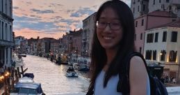 Nicole Kan smiling by a canal at sunset in Venice, wearing a white top and denim shorts, with a backpack.