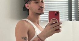 Young man posing in a tank top and cap, featuring a striking snake tattoo on his arm, reflecting a casual style.