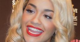 Rita Ora smiles brightly while being interviewed, showcasing her glamorous style at a music event.