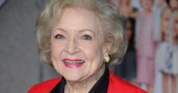 Betty White smiles warmly at a red carpet event, wearing a vibrant red blouse and a decorative brooch.