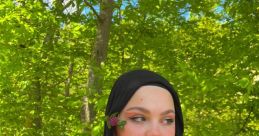 Young woman in black hijab surrounded by greenery, showcasing a delicate flower, reflecting nature's beauty.