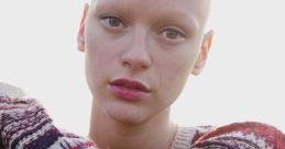 Bald model Joelle Rasmussen poses thoughtfully in a cozy, patterned sweater against a bright, natural backdrop.