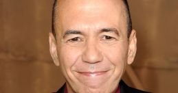 Gilbert Gottfried smiling in a black suit and burgundy shirt at a public event, showcasing his signature comedic style.