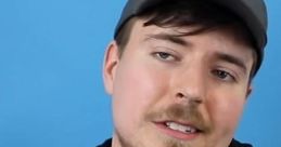 MrBeast in a black hoodie with "BEAST" text, wearing a cap, smiling against a blue background. Popular YouTuber.