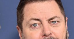 Nick Offerman poses with a serious expression, showcasing his well-groomed beard and stylish attire against a blue backdrop.