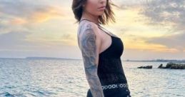 Loida Soriano poses stylishly on rocky shore at sunset, showcasing her unique fashion and tattoo artistry.