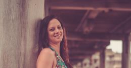 Pregnant woman in a colorful dress smiling, posing gracefully under a pier on a sandy beach, celebrating motherhood.