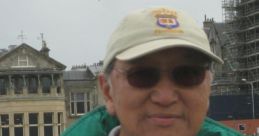 Chang Kuldee enjoying a day outdoors at a golf course, wearing a sporty jacket and cap, with historic buildings in the background.