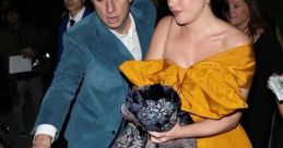 Florence Zack in a vibrant yellow dress, being assisted by a gentleman, exiting a venue during a nighttime event.