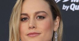 Brie Larson at a red carpet event, wearing elegant earrings and a stylish white dress, showcasing her sophisticated look.