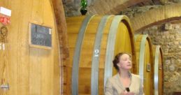 Giusy De Marco presenting in a wine cellar with large wooden barrels, showcasing her expertise in winemaking.