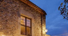 Cozy stone terrace of MASIA4, illuminated at dusk, featuring a dining table and inviting outdoor ambiance. Perfect for gatherings.