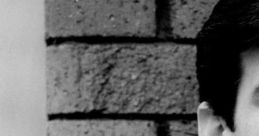 Close-up of a young man with dark hair and a light suit, set against a textured brick wall, evoking a thoughtful mood.