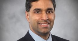 Portrait of Mahish Bhatia in a suit, smiling confidently against a gray backdrop, embodying professionalism and approachability.