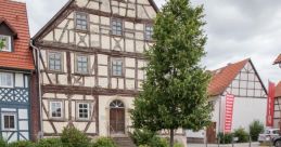 Historic half-timbered house with a green lawn and modern bench in a quaint area, showcasing Hubert Heinisch GmbH’s design influence.