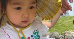 Adorable child in embroidered white dress and yellow sun hat, enjoying a sunny day outdoors with a loved one.