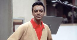 Stylish young man in a beige cardigan and red shirt stands confidently in a recording studio, capturing a vintage vibe.